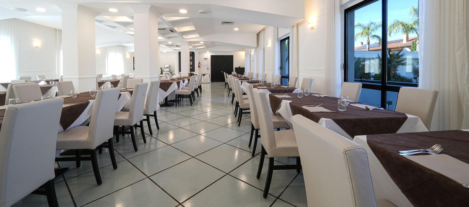 Elegante sala da pranzo con tavoli apparecchiati e ampie finestre luminose.