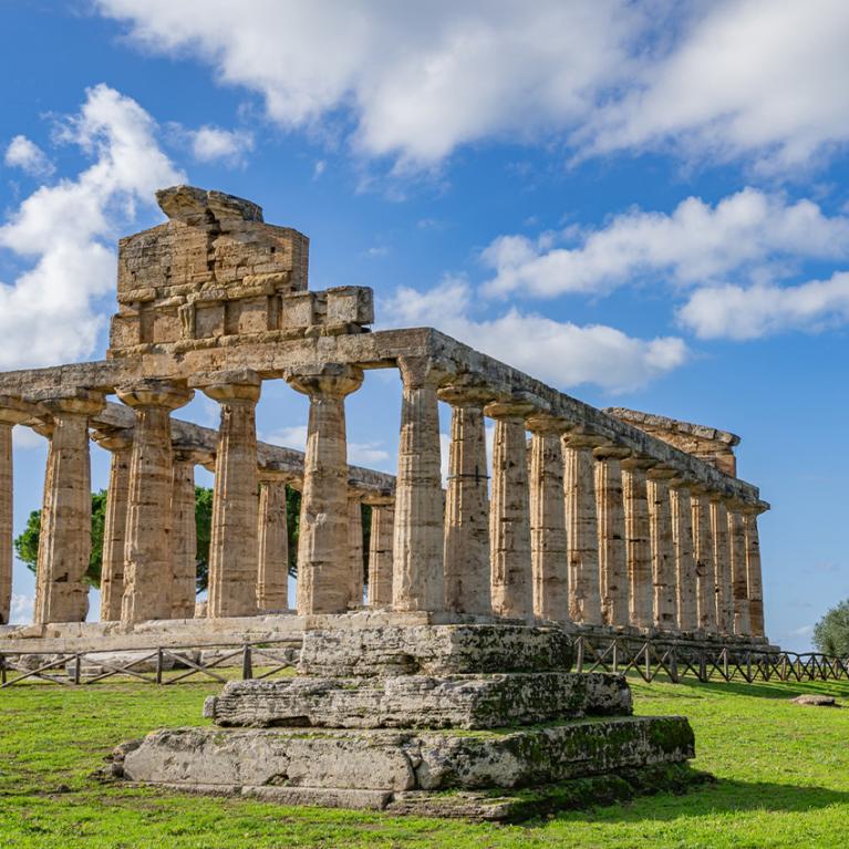 Tempio antico con colonne doriche, cielo blu e nuvole sullo sfondo.