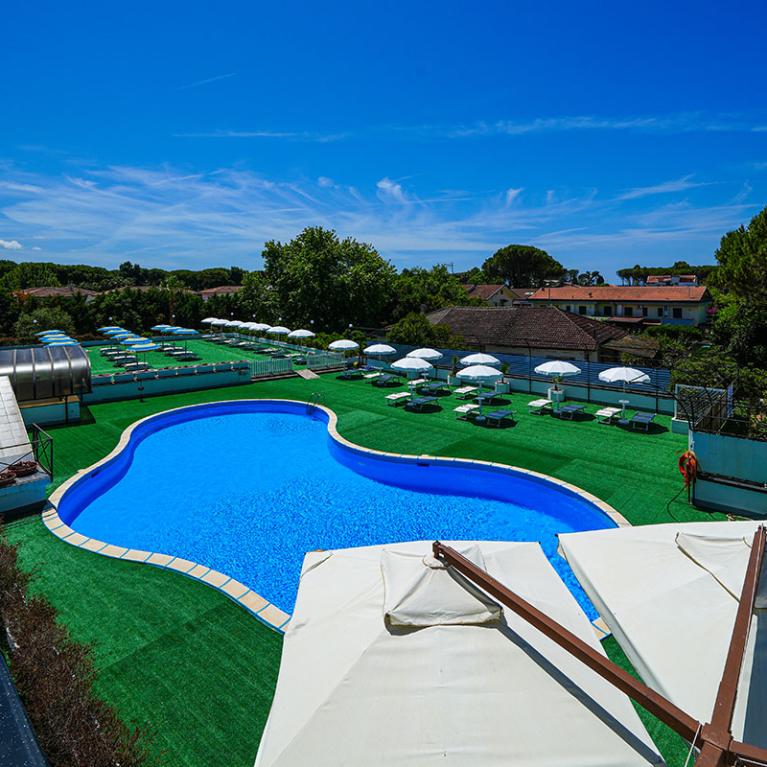 Piscina all'aperto con ombrelloni e lettini, circondata da un ampio giardino verde.