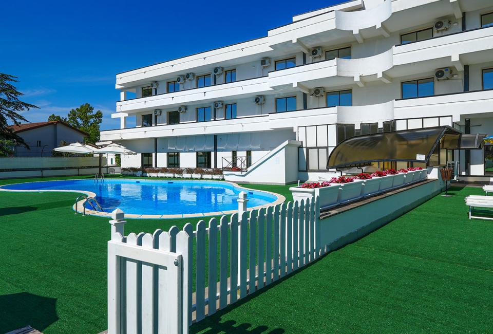 Modern hotel with pool, umbrellas, and green relaxation area.